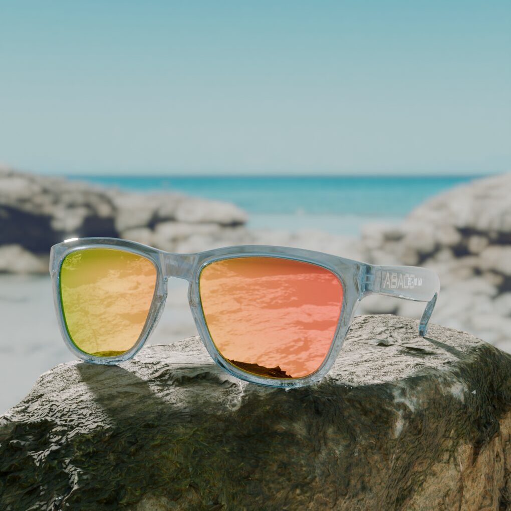 3D render of sunglasses with orange mirror lenses on a seaside rock